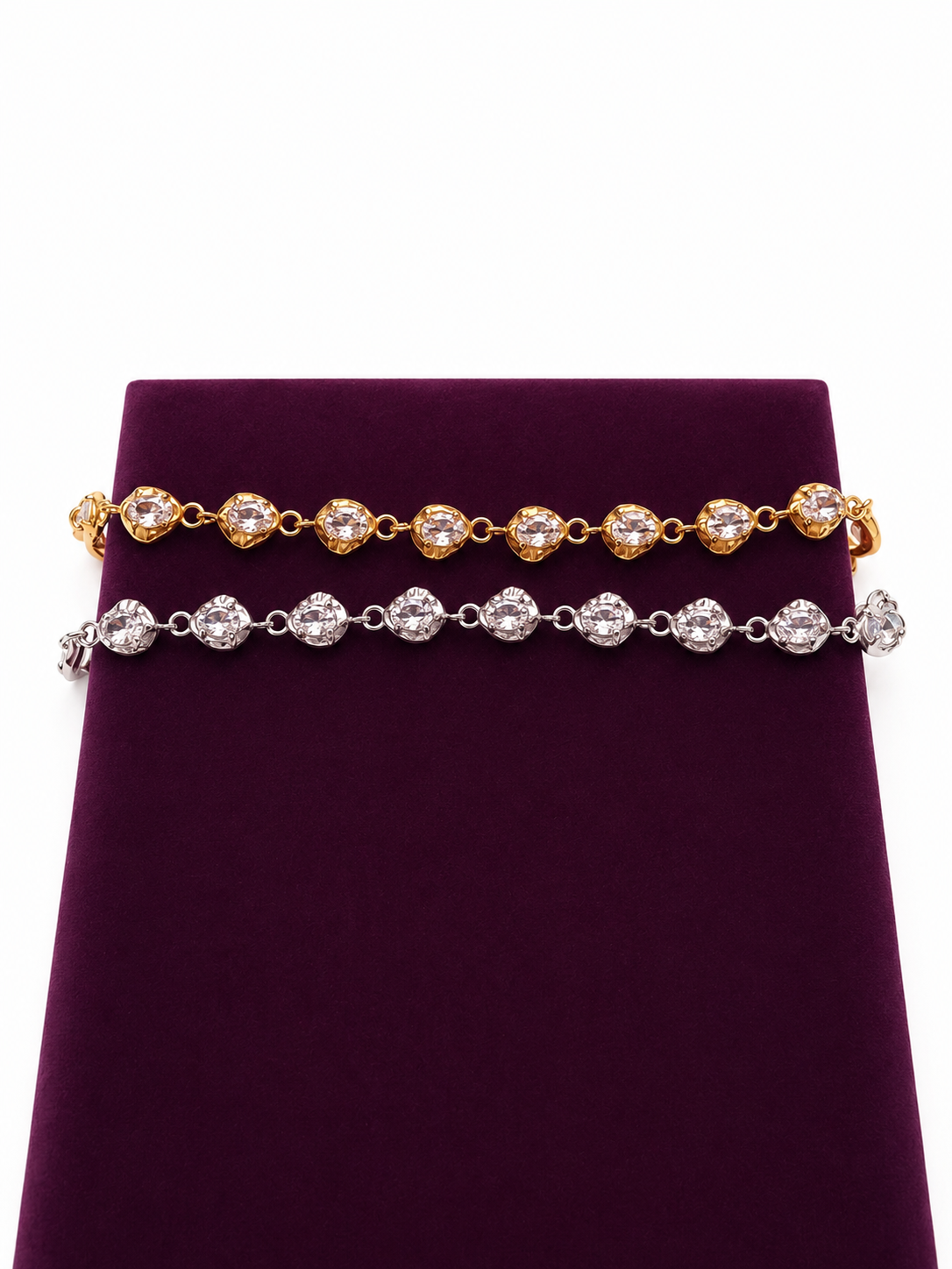 Two zircon bracelets displayed on a dark purple velvet jewelry stand against a white background. The top bracelet is 18K gold-plated with oval-cut zircons, and the bottom bracelet is silver-toned with oval-cut zircons.